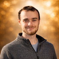 Porträt von Thomas Bella MSc BSc vor blauem Himmel, freundlich lächelnd mit kurzem Bart und sportlicher Jacke - Tech Lead Cyber Security aus Österreich.